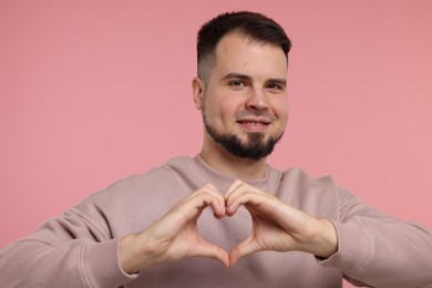 Man showing heart gesture with hands on pink background