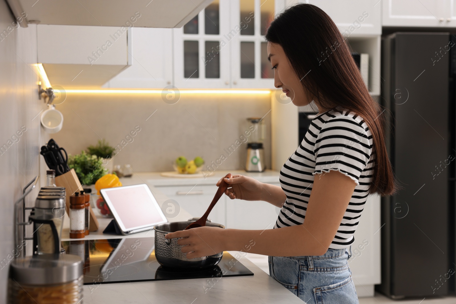 Photo of Beautiful woman cooking soup on cooktop in kitchen