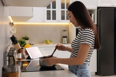 Beautiful woman cooking soup on cooktop in kitchen
