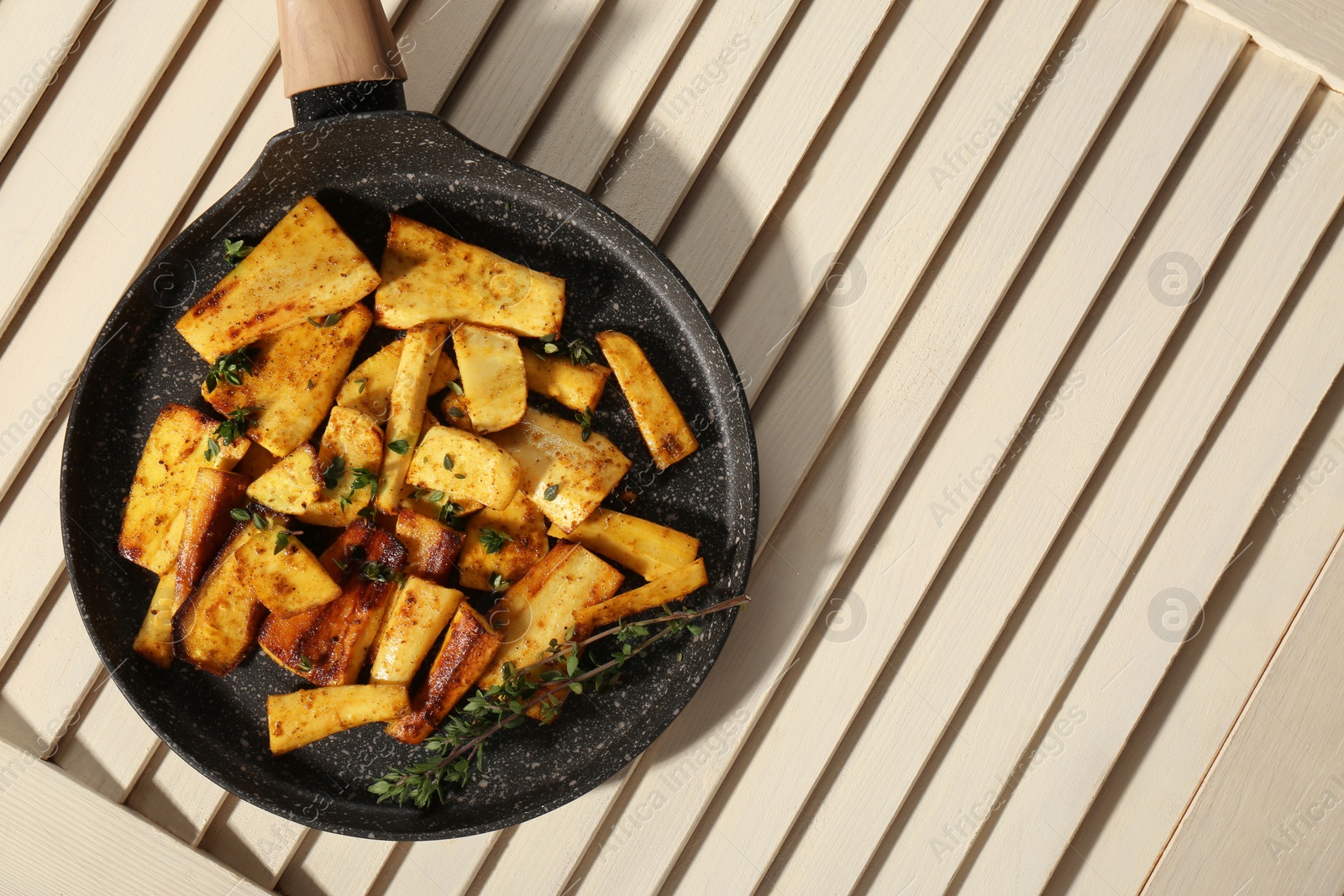 Photo of Delicious parsnips with thyme in frying pan on white wooden table, top view. Space for text