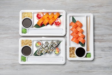 Food delivery. Plastic containers with delicious sushi, soy sauce, ginger, wasabi and chopsticks on light wooden table, flat lay