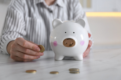 Photo of Woman with piggy bank and coin at marble table indoors, closeup