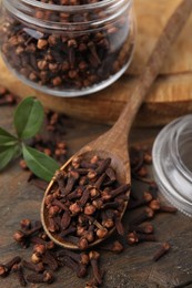 Photo of Glass jar and spoon with aromatic cloves on wooden table, above view