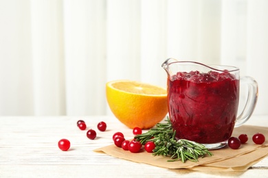 Photo of Tasty cranberry sauce in glass pitcher with rosemary and citrus fruit on table. Space for text