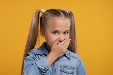 Photo of Embarrassed little girl covering her mouth with hand on orange background