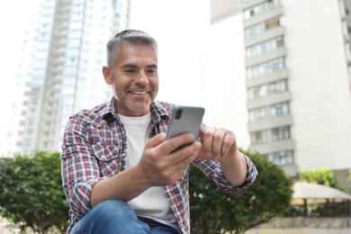 Portrait of handsome mature man using mobile phone in city center