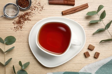 Freshly brewed rooibos tea, dry leaves and spices on wooden table, flat lay