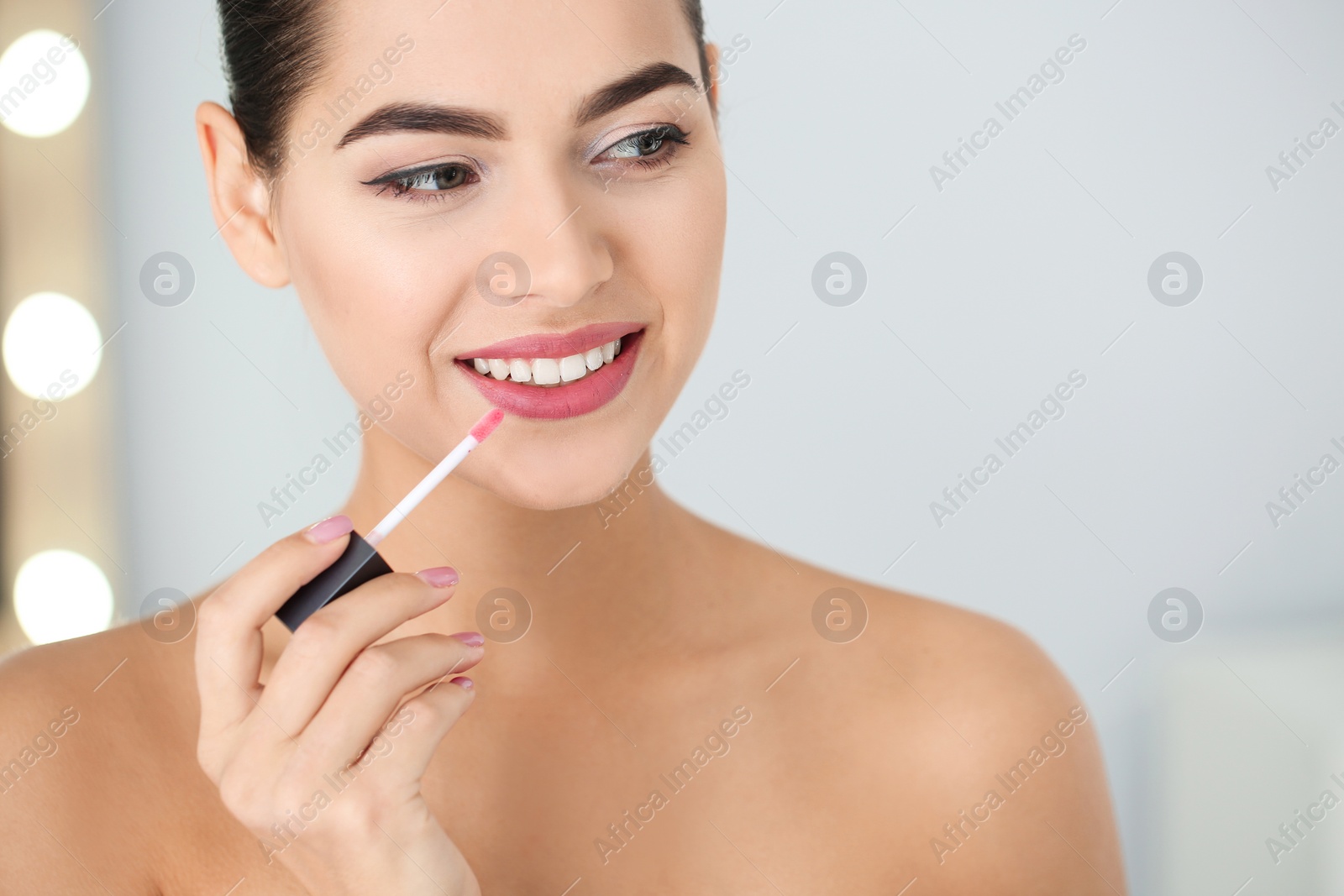Photo of Young woman applying liquid lipstick on blurred background. Space for text
