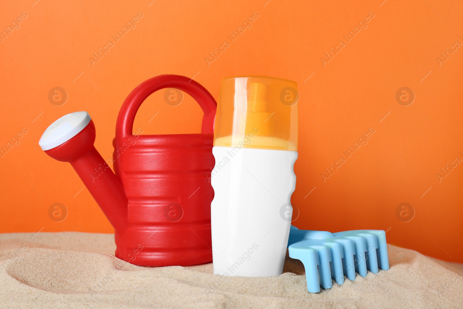 Photo of Suntan product and plastic beach toys on sand against orange background