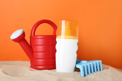 Photo of Suntan product and plastic beach toys on sand against orange background