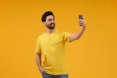 Photo of Smiling man taking selfie with smartphone on yellow background