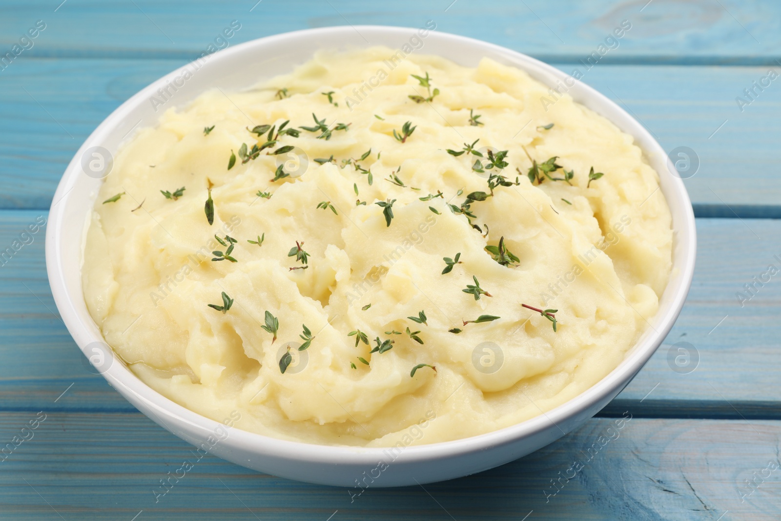Photo of Bowl of tasty mashed potato with rosemary on light blue wooden table, closeup