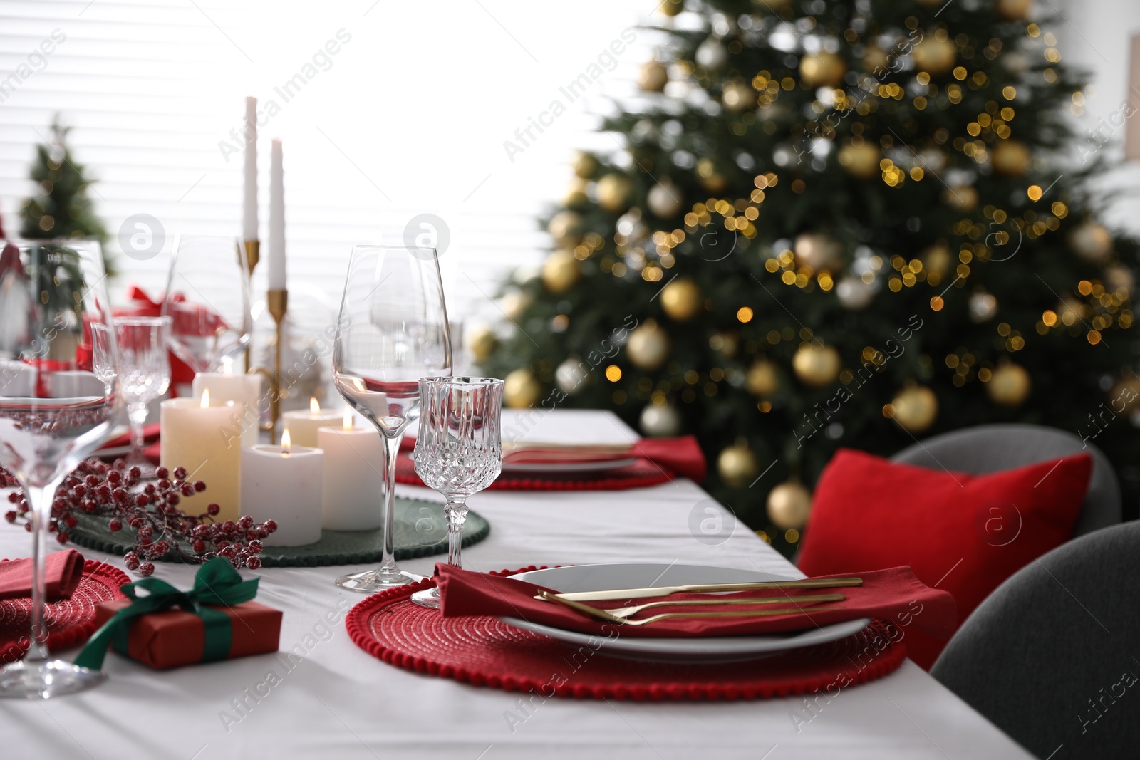 Photo of Christmas table setting with burning candles, gift box and dishware indoors