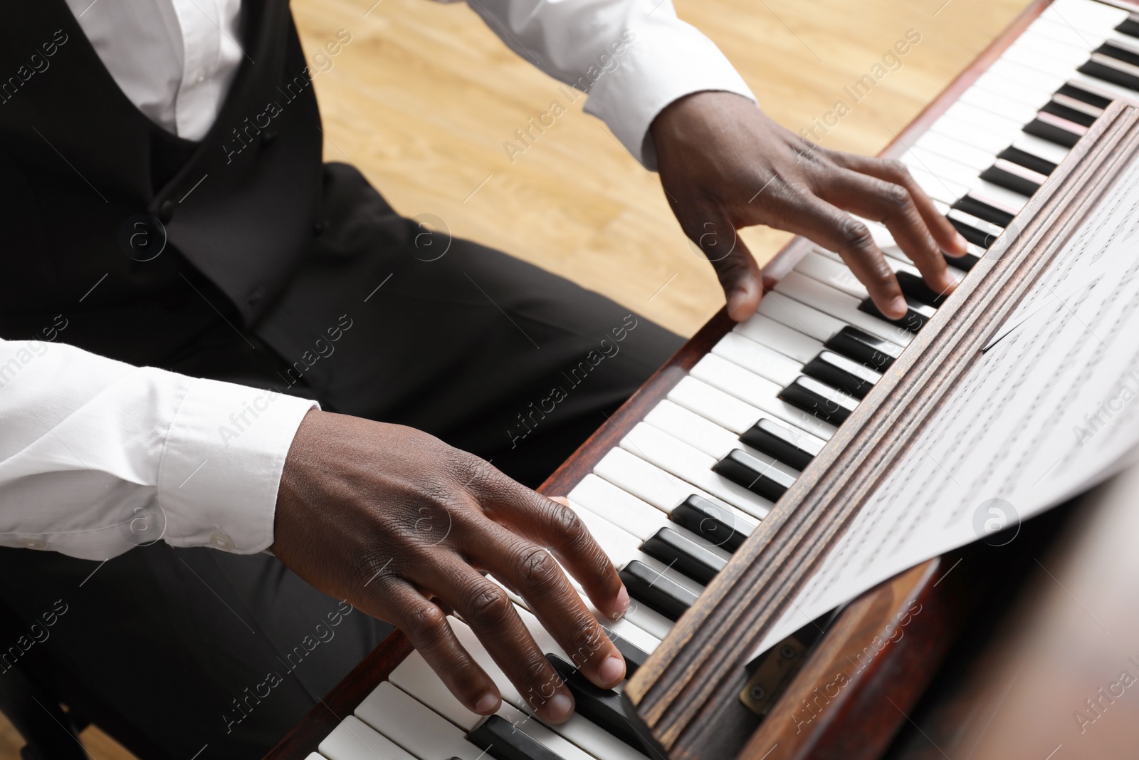 Photo of African-American man playing piano indoors, closeup. Talented musician