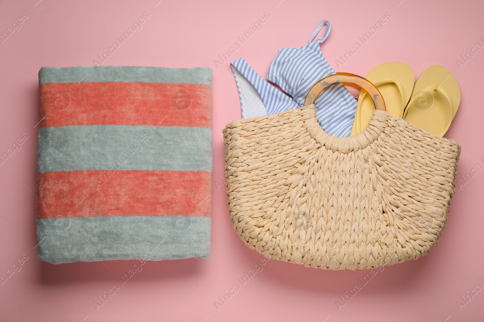 Photo of Beach bag with swimsuit, flip flops and towel on pink background, flat lay