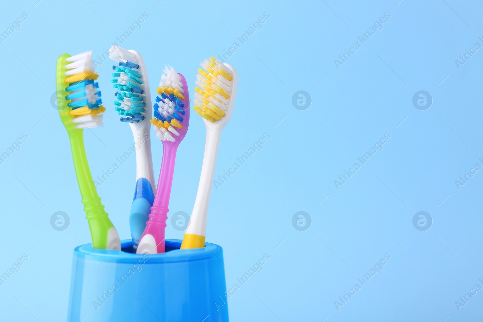 Photo of Different toothbrushes in holder on light blue background, closeup. Space for text