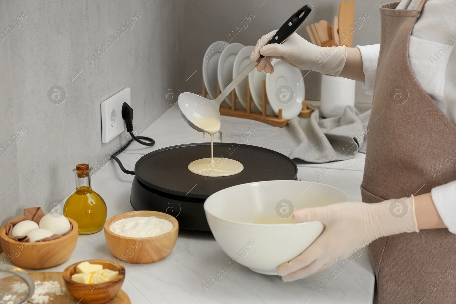 Photo of Woman cooking delicious crepe on electric pancake maker at white marble table in kitchen, closeup