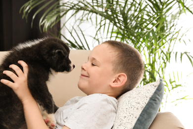 Photo of Little boy with Akita inu puppy on sofa at home. Friendly dog