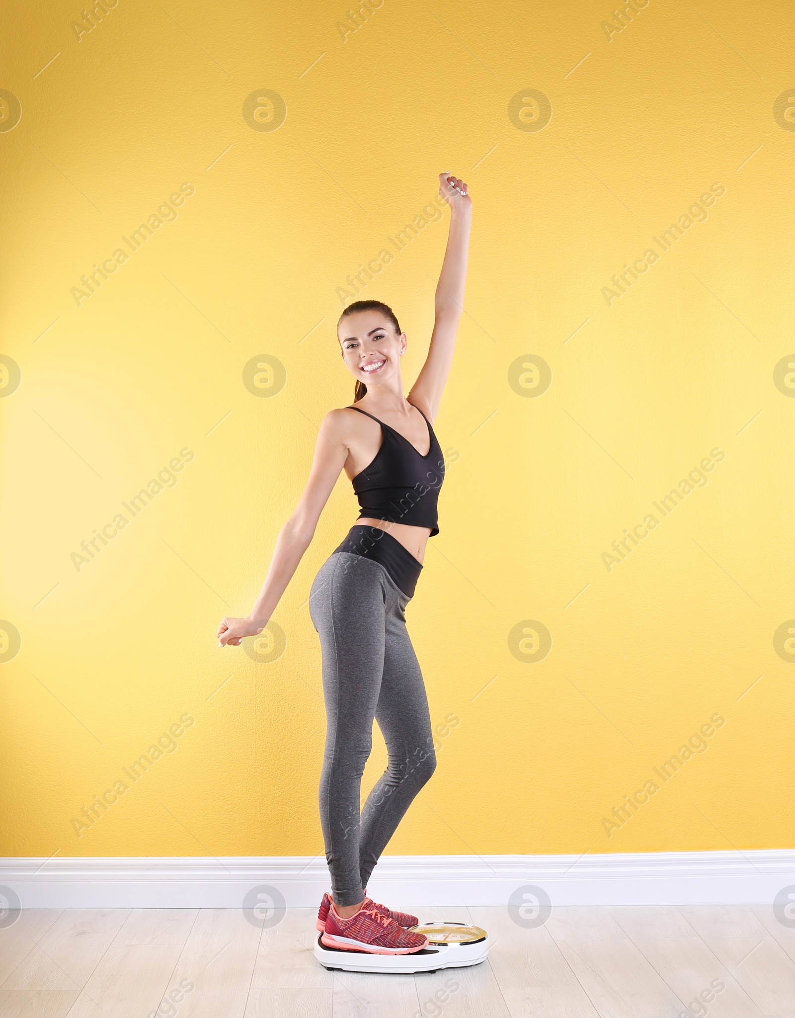 Photo of Happy young woman measuring her weight using scales near color wall. Weight loss motivation