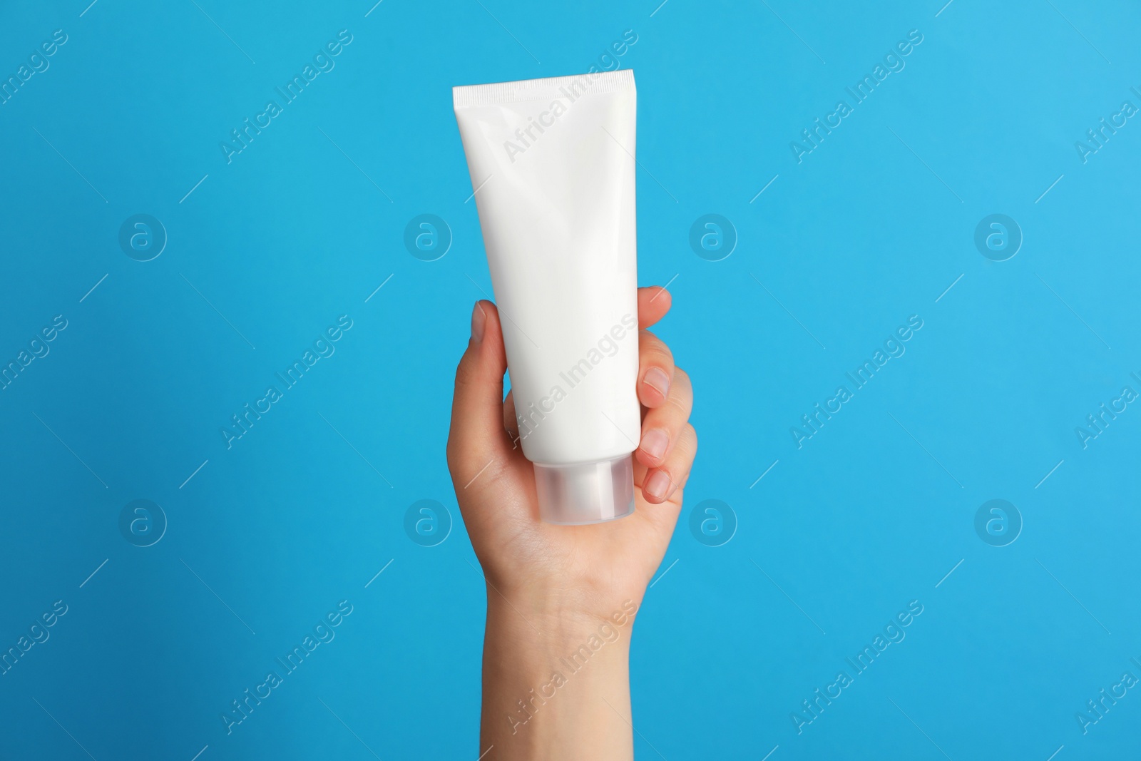 Photo of Woman holding tube of face cream on light blue background, closeup