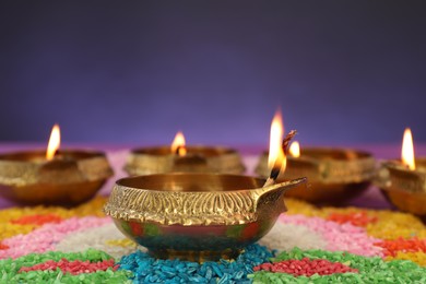 Diwali celebration. Diya lamps and colorful rangoli against purple background, closeup