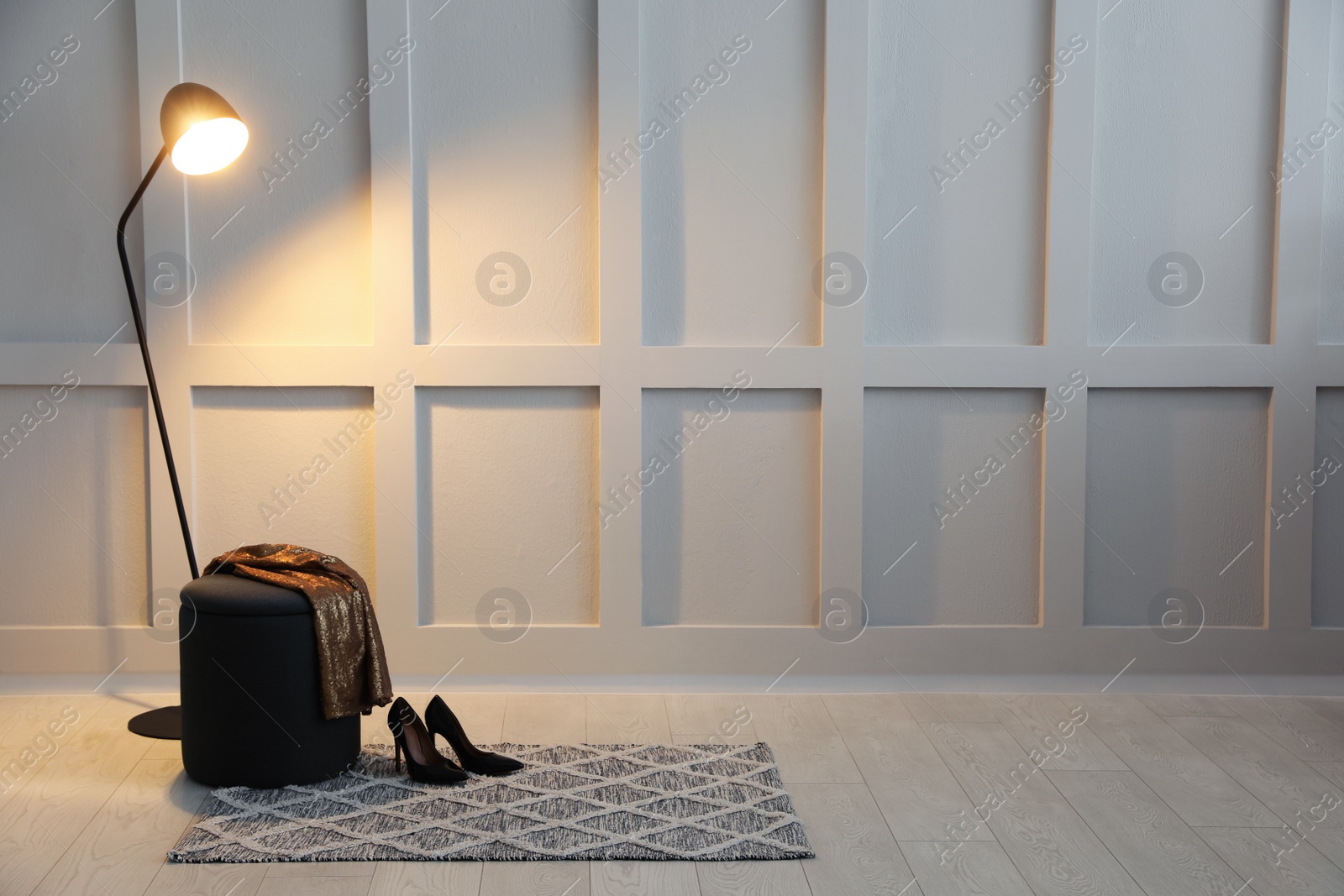 Photo of Stylish room interior with grey rug, ottoman and lamp near white wall. Space for text