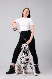 Beautiful young woman with her adorable Dalmatian dog on light grey background. Lovely pet