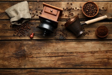 Photo of Vintage manual coffee grinder, beans, powder and jezve on wooden table, flat lay. Space for text