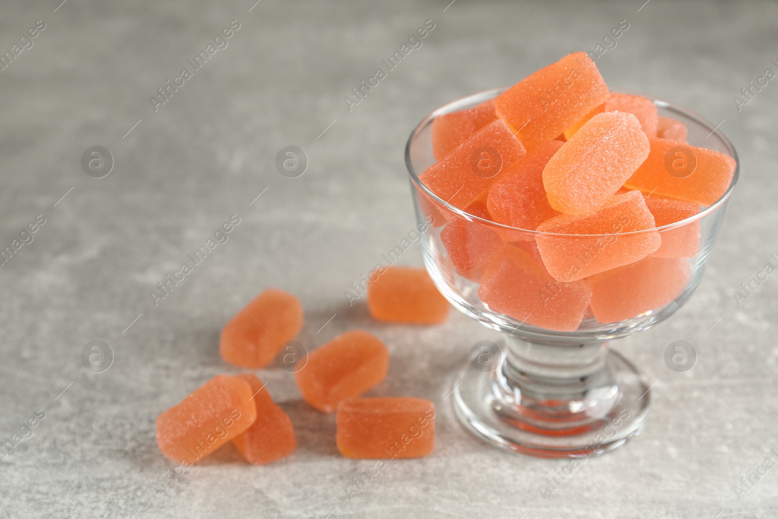 Photo of Tasty orange jelly candies in glass dessert bowl on grey table. Space for text