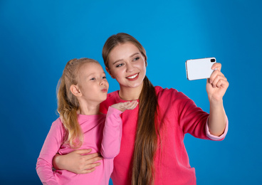 Photo of Happy mother and little daughter taking selfie on blue background