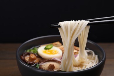 Eating delicious vegetarian ramen with chopsticks at table against black background, closeup