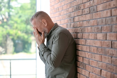 Photo of Senior man in state of depression near brick wall