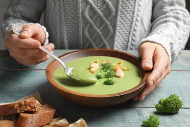 Photo of Woman eating fresh vegetable detox soup made of broccoli with croutons at table, closeup