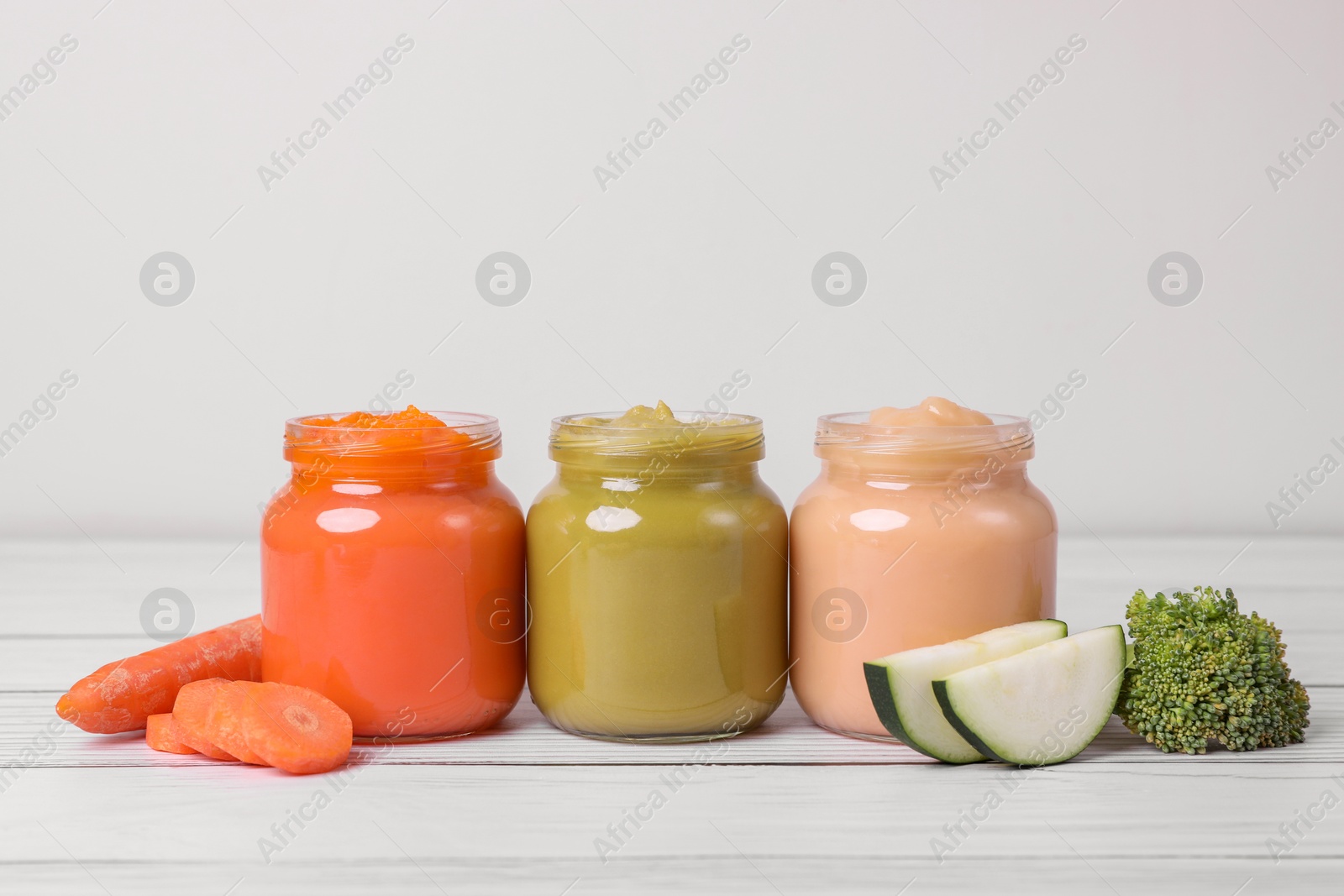 Photo of Jars of healthy baby food and vegetables on white wooden table