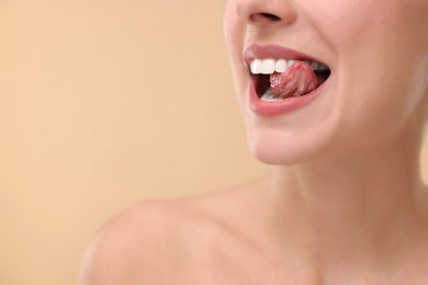 Photo of Woman with beautiful lips licking her teeth on beige background, closeup. Space for text