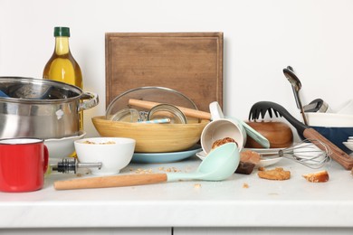 Many dirty utensils, dishware and food leftovers on white countertop. Mess in kitchen