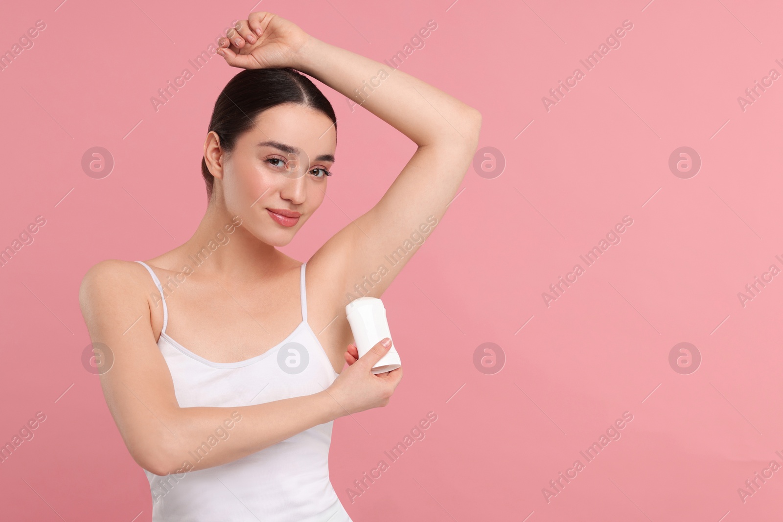 Photo of Beautiful woman applying deodorant on pink background, space for text