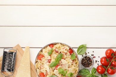 Plate of delicious pasta with tomatoes, basil and parmesan cheese near ingredients on white wooden table, flat lay. Space for text