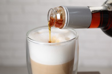 Photo of Pouring syrup into glass of tasty coffee on blurred background, closeup
