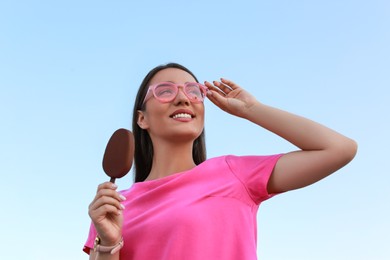 Photo of Beautiful young woman holding ice cream glazed in chocolate against blue sky, low angle view