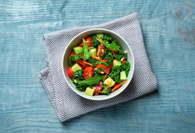 Photo of Tasty fresh kale salad on light blue wooden table, flat lay