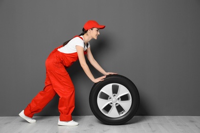 Photo of Female mechanic in uniform with car tire on grey wall background