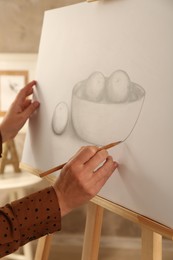 Photo of Woman drawing bowl of fruits with graphite pencil on canvas indoors, closeup
