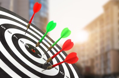 Image of Board with color darts hitting target against blurred view of cityscape