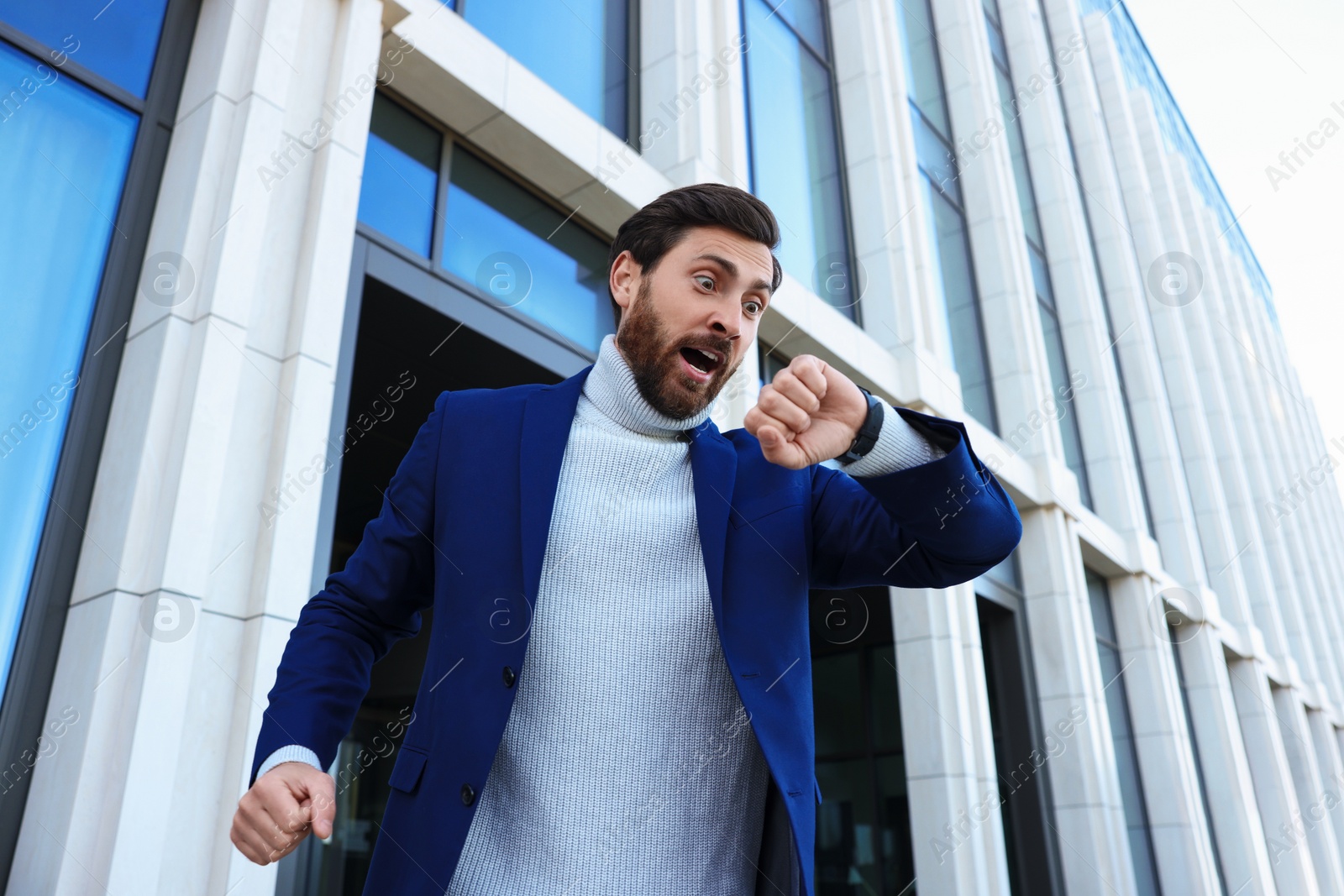 Photo of Emotional businessman looking at watch near building, low angle view. Being late concept