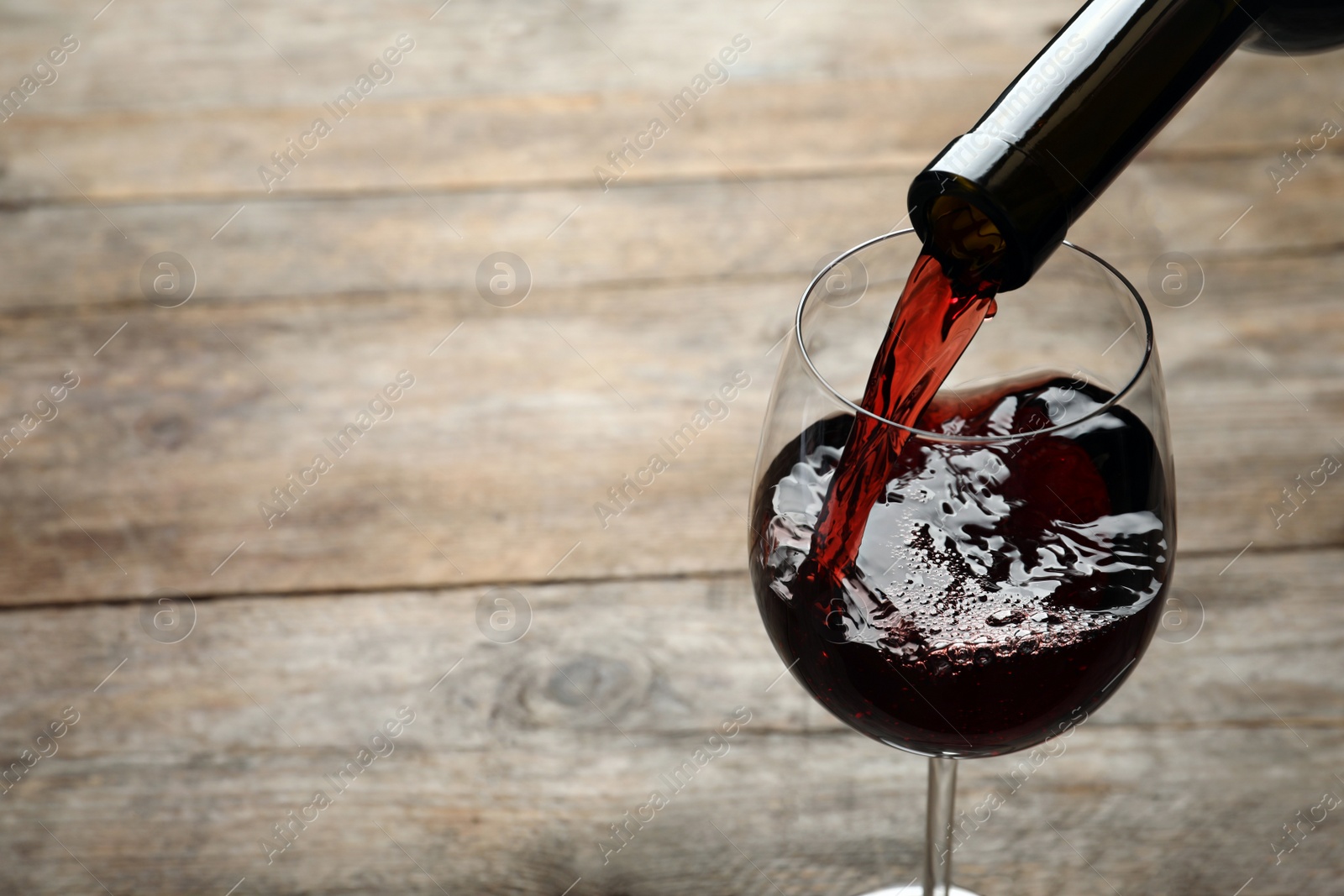 Photo of Pouring red wine from bottle into glass on wooden background. Space for text