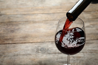 Pouring red wine from bottle into glass on wooden background. Space for text