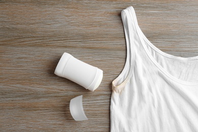 White undershirt with stain and deodorant on wooden background, top view