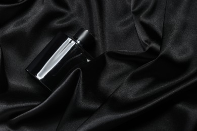 Photo of Luxury men's perfume in bottle on black satin fabric, top view. Space for text