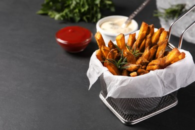 Photo of Frying basket with sweet potato fries and sauces on black table. Space for text